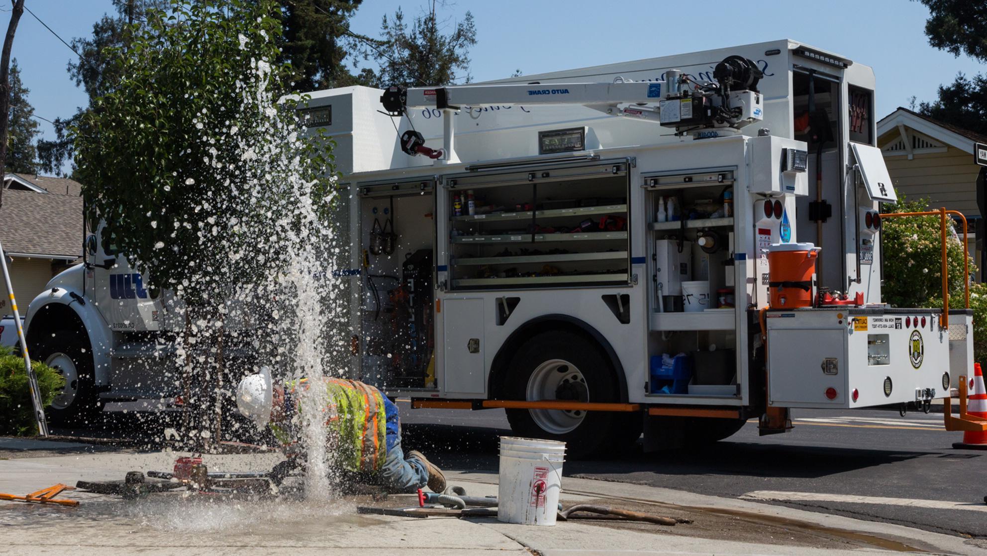 Worker kneeling down to fix a leak spraying water out of the ground